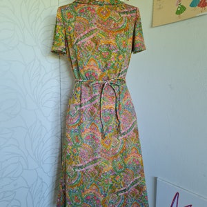 Pu&ograve; includere: Un abito vintage con stampa paisley in tonalit&agrave; di verde, rosa, arancio e giallo. L'abito ha un collo alto, maniche corte e una cintura con lacci.