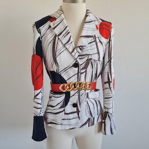 May include: A patterned blazer with a red belt and gold chain buckle. The blazer features a white background with black and brown abstract designs and red accents. The sleeves have black cuffs.