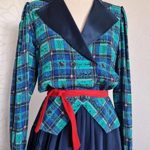 May include: A blue and green plaid dress with a black satin collar and a red sash. The dress has a fitted bodice and a full skirt.