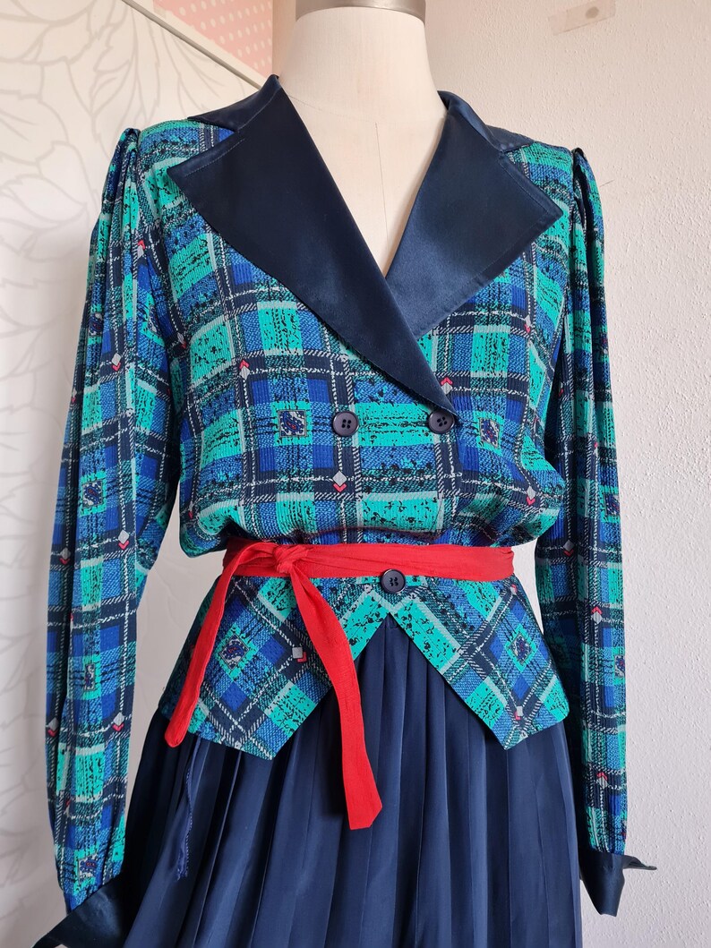 May include: A blue and green plaid dress with a black satin collar and a red sash. The dress has a fitted bodice and a full skirt.