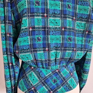 May include: A blue and green plaid blouse with a gathered waist. The blouse has long sleeves and a button-up front.
