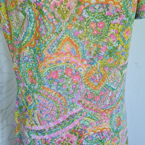 Pu&ograve; includere: Un abito vintage con una stampa paisley colorata con sfumature di rosa, verde, arancione e blu. Il tessuto presenta un motivo floreale con piccoli fiori in tutto.