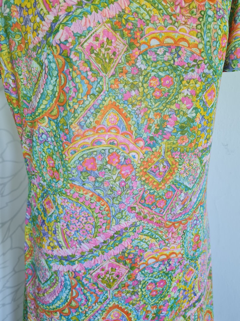 Pu&ograve; includere: Un abito vintage con una stampa paisley colorata con sfumature di rosa, verde, arancione e blu. Il tessuto presenta un motivo floreale con piccoli fiori in tutto.