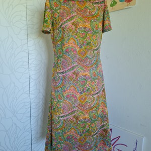 Pu&ograve; includere: Un abito vintage con stampa paisley in tonalit&agrave; di verde, rosa, arancio e giallo. L'abito ha un collo alto e maniche corte.