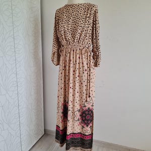 Puede incluir: Un vestido largo de maxi beige con estampado de lunares negros. El vestido tiene una cintura fruncida y un estampado floral en el dobladillo inferior.