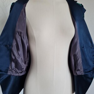 May include: A navy blue cropped jacket with a green and blue patterned lining. The jacket has a collar and buttons.