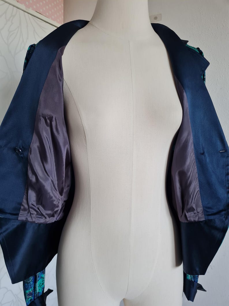 May include: A navy blue cropped jacket with a green and blue patterned lining. The jacket has a collar and buttons.