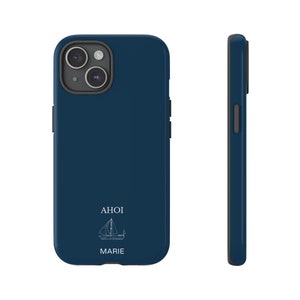 Puede incluir: Una funda de smartphone azul oscuro con un dibujo lineal blanco de un velero, el texto AHOI y el nombre MARIE impresos en la parte posterior. La funda incluye un recorte para la c&aacute;mara con borde negro y una vista lateral del perfil.