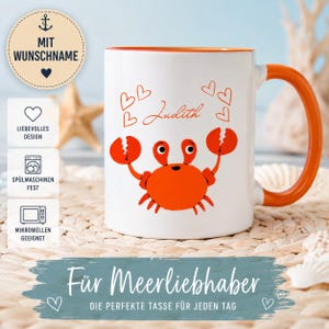 May include: A white ceramic mug with an orange interior and handle, featuring a red crab illustration, several red heart outlines, and the name Judith printed in red script. The mug displays text in German regarding customization and care.