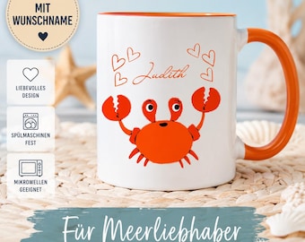 Puede incluir: Una taza de cerámica blanca con interior y asa de color naranja, que presenta una ilustración de un cangrejo rojo, varios corazones rojos y el nombre Judith impreso en letra cursiva roja. La taza muestra texto en alemán sobre personalización.