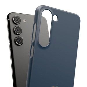 May include: A dark gray smartphone with three rear camera lenses positioned next to a solid navy blue protective phone case. The case features a large vertical cutout for the camera array and smaller side cutouts for buttons and ports.