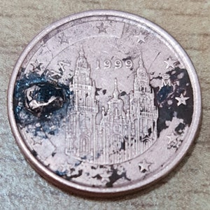 Könnte beinhalten: Eine 1-Cent-Euro-Münze aus Kupfer mit einer Abbildung der Kathedrale von Santiago de Compostela in Spanien. Die Münze trägt das Jahr 1999 und 12 Sterne am Rand.