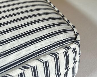 May include: Close-up of a rectangular cushion with a cream-colored background and navy blue stripes. The cushion has a piped edge and a herringbone weave pattern. The stripes run horizontally across the cushion.
