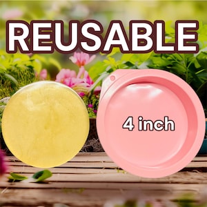 Op de afbeelding: De afbeelding toont twee items: een rond, geel object en een roze, cirkelvormige container. De container is gemarkeerd met "4 inch" (ongeveer 10 cm) in witte tekst. Het woord "REUSABLE" staat in grote witte letters erboven. De achtergrond toont groen en bloemen.