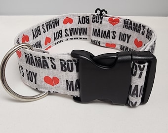 May include: White dog collar with a black buckle and a silver D-ring. The collar is printed with the words "Mama's Boy" and red hearts.