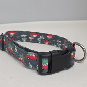 Op de afbeelding: Een grijze hondenriem met een feestelijk patroon van rode auto's met kerstbomen en groene bomen. De riem heeft een zwarte plastic gesp en een zilveren metalen D-ring.