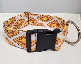 Puede incluir: Un collar para perros con un estampado repetido de gofres con mantequilla sobre un fondo blanco. Tiene una hebilla de plástico negro y una anilla en D de metal plateado para sujetar la correa. Diseñado para mascotas.