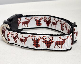 May include: A white dog collar with a black buckle and a silver metal ring. The collar features a repeating pattern of red and black plaid deer heads and deer silhouettes.