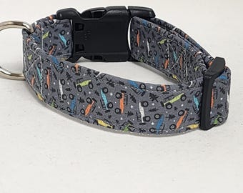 May include: A gray dog collar with a repeating pattern of colorful trucks. The collar has a black plastic buckle and a silver D-ring.
