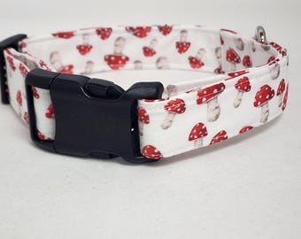 May include: White dog collar with a red and white mushroom print. The collar has a black plastic buckle.