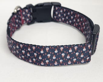 May include: Navy blue dog collar with a repeating pattern of white snowmen and red accents. The collar has a black plastic buckle and a metal loop for attaching a leash. A festive accessory for pets.