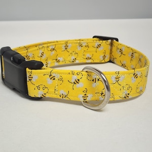 May include: Yellow dog collar with a black buckle and silver D-ring. The collar is covered in a repeating pattern of small, silver glitter bees.