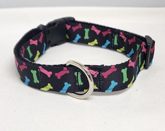 May include: Black dog collar with a colorful bone pattern. The collar has a silver metal D-ring and a black plastic buckle.