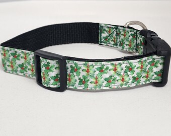 May include: A white dog collar with a green and red holly pattern. The collar has a black buckle and a silver metal clasp.