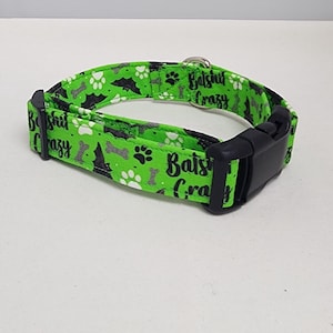 Puede incluir: Collar de perro verde con un estampado en blanco y negro de murciélagos, huellas de patas y huesos. El collar tiene el texto "Bats**t Crazy" impreso.