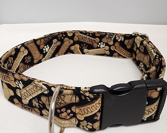 May include: A black dog collar with a brown and tan print of bones and paw prints. The collar has a black plastic buckle and a silver D-ring.