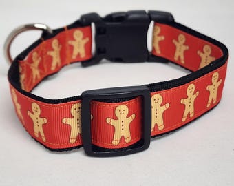 May include: Red dog collar with a gingerbread man pattern. The collar has a black buckle and a silver D-ring.