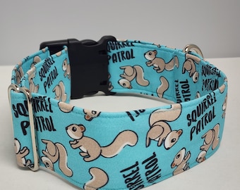 May include: A turquoise blue dog collar with a black buckle and silver D-ring. The collar has a repeating pattern of brown squirrels and the text "Squirrel Patrol".