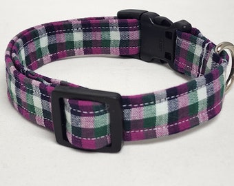 May include: A dog collar with a plaid pattern in shades of purple, green, and white. The collar has a black plastic buckle and a metal D-ring for leash attachment. The fabric is stitched with white thread.