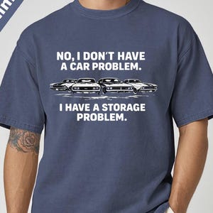 May include: Denim blue t-shirt with the text "NO, I DON'T HAVE A CAR PROBLEM. I HAVE A STORAGE PROBLEM." and a graphic of classic cars. The shirt is a relaxed fit.