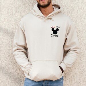 May include: A beige hoodie with a black Mickey Mouse head and the text "Disney 2025" above the head and "JAMES" below the head.