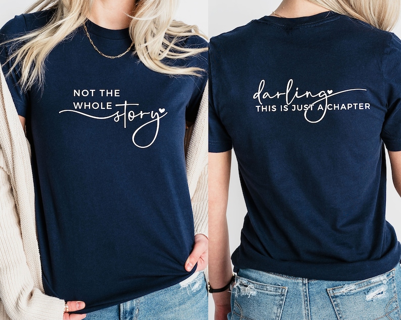 May include: A navy blue t-shirt with the text "Not the whole story" on the front and "Darling, this is just a chapter" on the back. Both phrases are written in a cursive font with a small heart symbol.