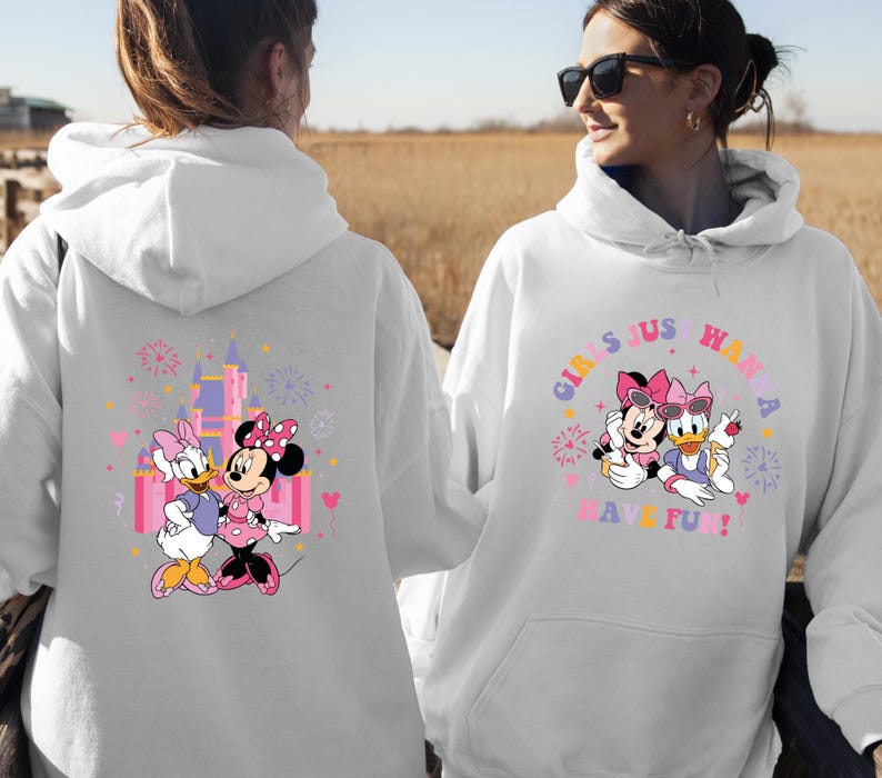 K&ouml;nnte beinhalten: Wei&szlig;er Kapuzenpullover mit einem farbenfrohen Aufdruck von Minnie Mouse und Daisy Duck. Auf der Vorderseite des Sweatshirts steht der Text "GIRLS JUST WANNA HAVE FUN!". Auf der R&uuml;ckseite des Sweatshirts befindet sich eine Schlossgrafik.