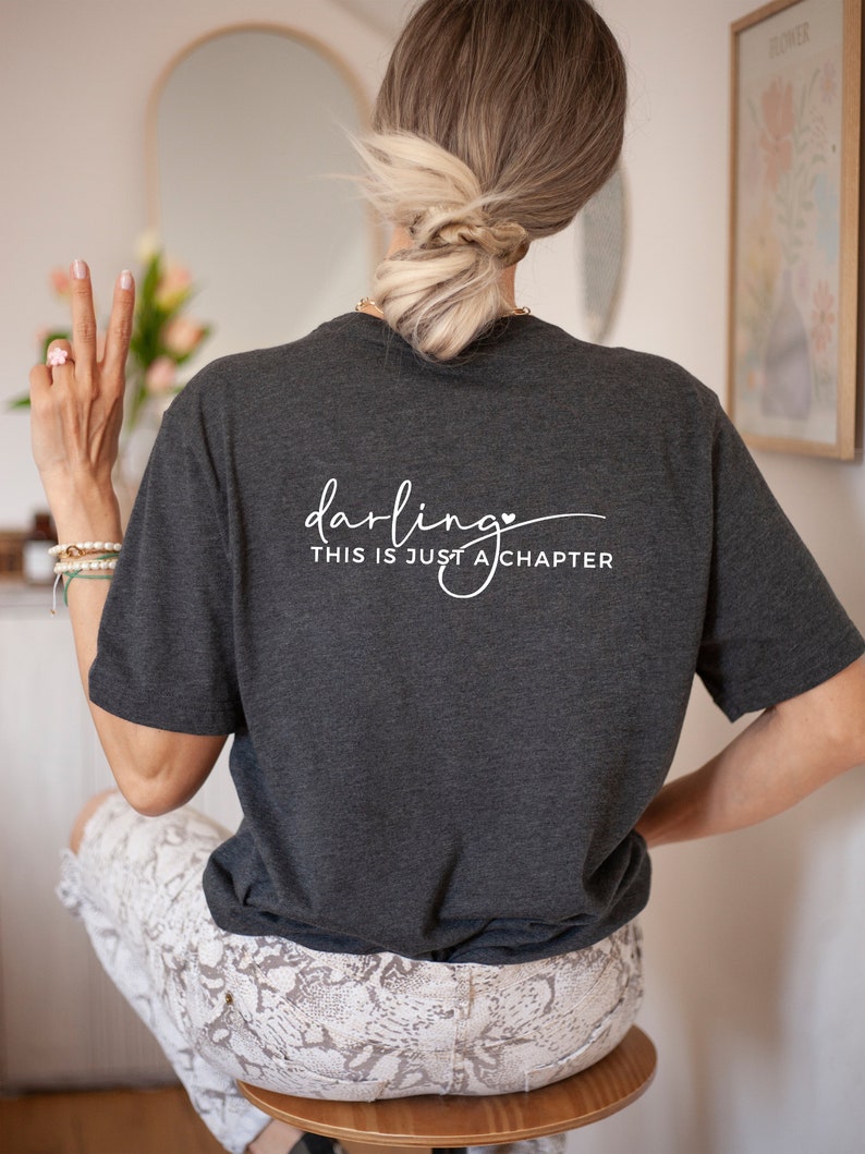 May include: A dark gray t-shirt with the text "darling this is just a chapter" in white lettering with a small heart symbol.