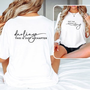 May include: White t-shirt with the text "darling, this is just a chapter" on the back and a small heart symbol. A second white t-shirt with the text "not the whole story" and a small heart symbol is shown on a model.