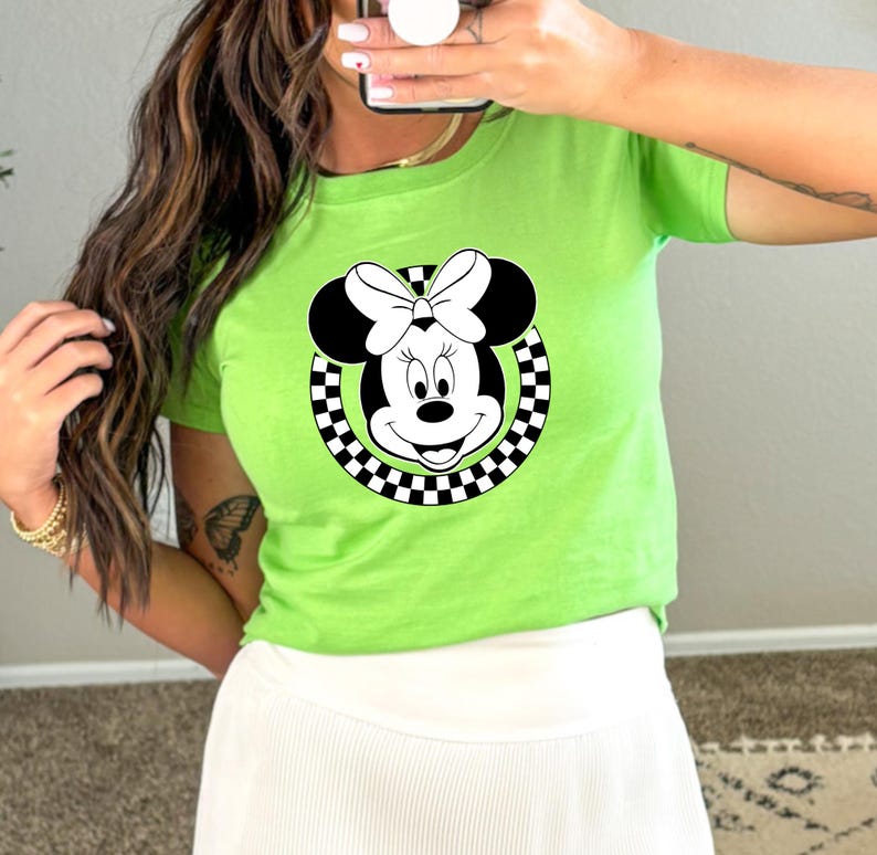May include: A green t-shirt with a black and white checkered circle around a cartoon image of Minnie Mouse. Minnie Mouse is wearing a black bow.