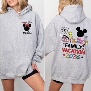 May include: Gray hooded sweatshirt with a Mickey Mouse design on the back. The design includes the text "Disney Family Vacation 2025" and colorful fireworks. The front of the sweatshirt has a smaller Mickey Mouse design with the text "Disney 2025" and "Monica".
