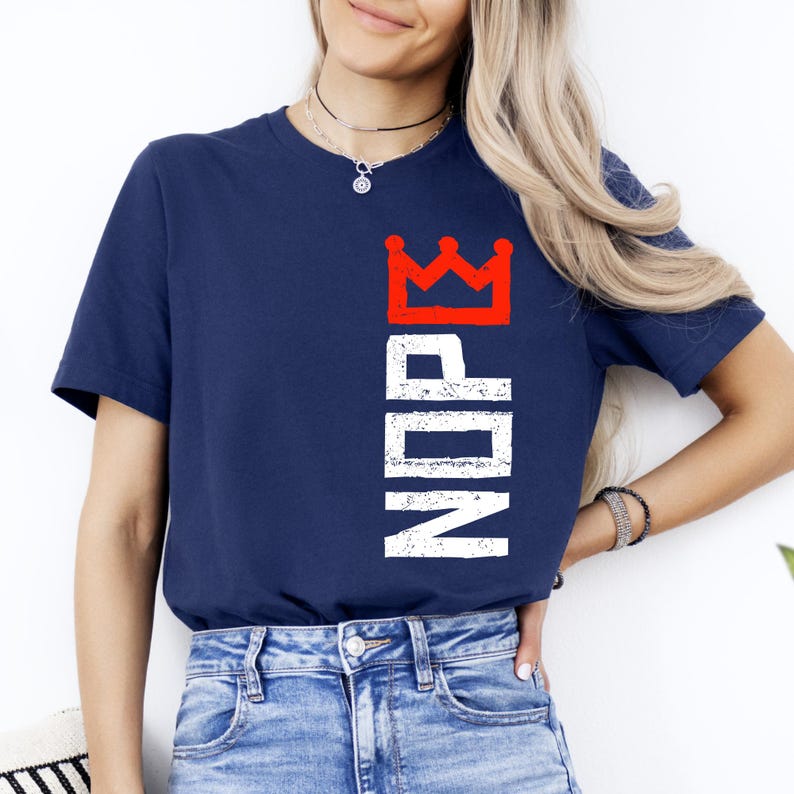 May include: Navy blue t-shirt with the word "NDPE" in white vertical text and a red crown graphic. The t-shirt is a crew neck style.