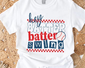 May include: White t-shirt with a baseball-themed graphic. The design features the words "hey BATTER batter SWING" in blue and red, with a baseball illustration. The shirt has a crew neck and short sleeves.