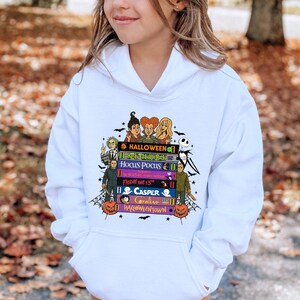 May include: White hoodie with a colourful graphic of stacked books, each with a Halloween film title and characters. The design includes pumpkins, bats, and the word "HALLOWEEN".