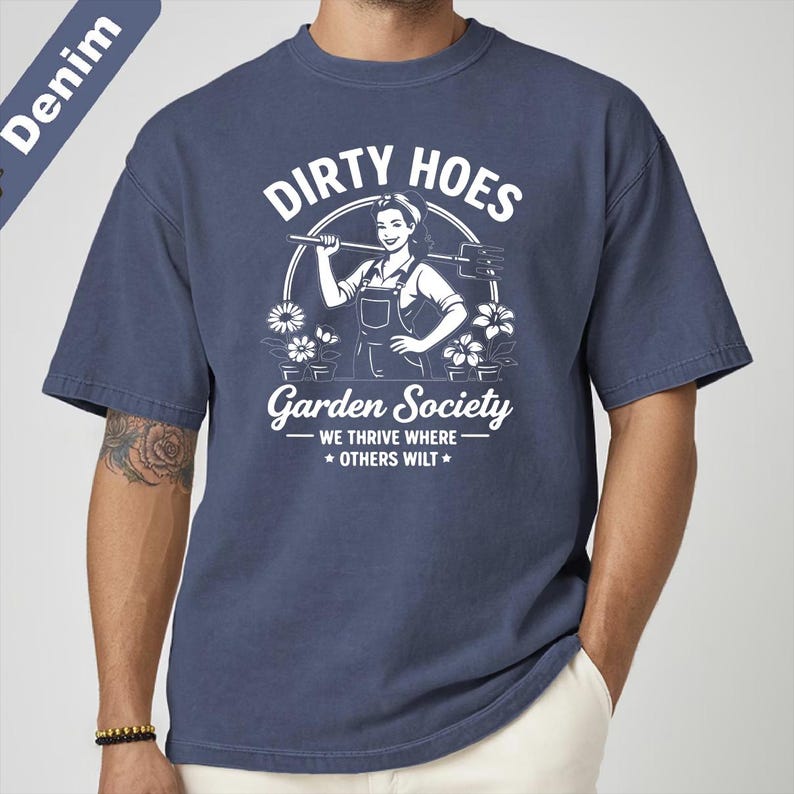 May include: Denim blue t-shirt with a white graphic that reads "Dirty Hoes Garden Society" featuring a woman with a gardening tool. The text "We thrive where others wilt" is also included in the design.