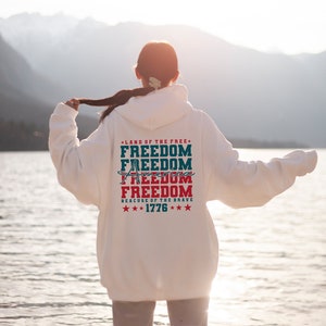 May include: White hooded sweatshirt with a red, white and blue graphic print that says "Land of the Free, Freedom, Freedom, Freedom, Freedom, Because of the Brave, ***1776***".