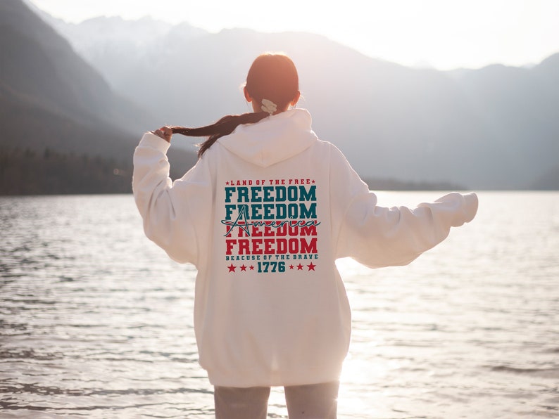 May include: White hooded sweatshirt with a red, white and blue graphic print that says "Land of the Free, Freedom, Freedom, Freedom, Freedom, Because of the Brave, ***1776***".