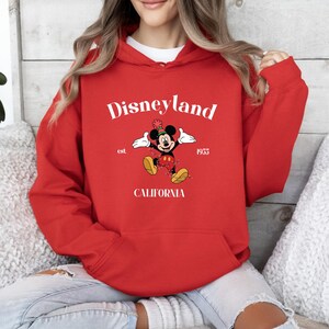 Op de afbeelding: Rood hoodie met een witte afbeelding van Mickey Mouse met een feestmuts, de tekst "Disneyland est. 1955 Californi&euml;" en een rood-zwart stippenpatroon.