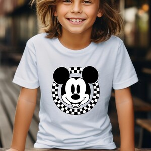 May include: White t-shirt with a black and white checkered circle around a black and white cartoon Mickey Mouse face.
