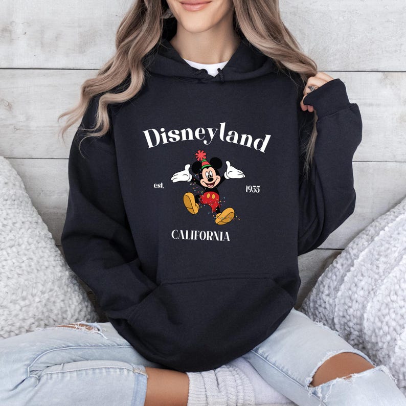 Op de afbeelding: Zwarte hoodie met een witte afbeelding van Mickey Mouse met een feestmuts en de tekst "Disneyland est. 1955 Californi&euml;".